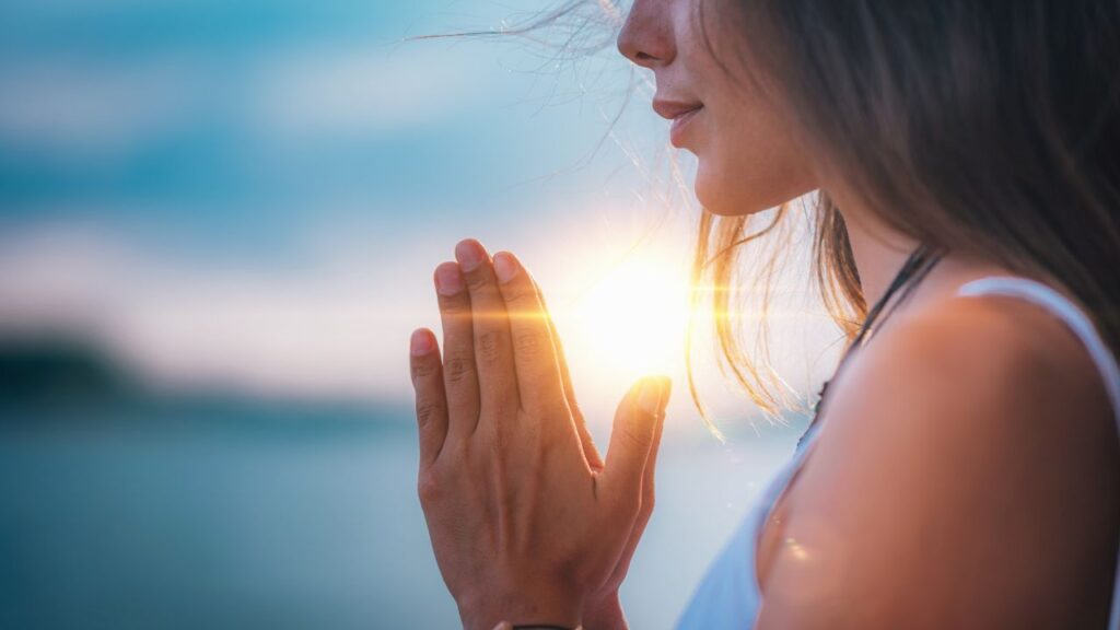 スピリチュアルな神さまとのご縁を祈り太陽の光の前で手を合わせて祈る女性